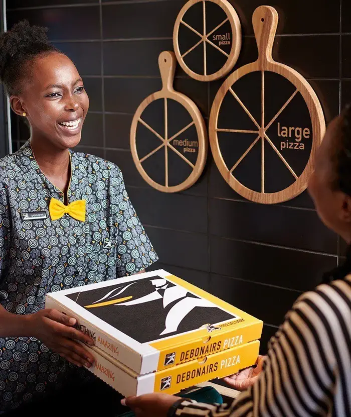 Debonairs Pizza employee handing pizza takeaway boxes to a customer